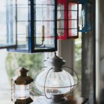 Assortment of colorful handcrafted lanterns in red, blue, and metallic finishes displayed in a sunlit window at Nauset Lantern Shop.