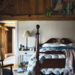Rustic bedroom with a four-poster bed, wood-paneled ceiling, and vintage artwork above the headboard