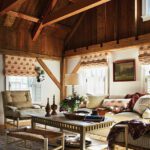 Warm living room with exposed timber beams, floral window treatments, and layered seating around a central coffee table