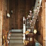 Welcoming entryway with raw plaster walls, a curved staircase, antique table, and a tall vase of cherry blossoms
