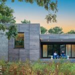 Contemporary cedar-clad home with clean lines, large glass doors, and a covered patio surrounded by native landscaping