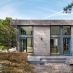 Back view of a modern coastal home with tall windows, outdoor shower, and spacious deck nestled among trees