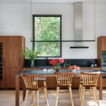Modern kitchen with walnut cabinetry, black countertops, and a central island with spindle-back stools beneath minimalist pendant lights