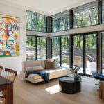 Bright living room with floor-to-ceiling windows, contemporary art, and neutral furnishings opening to the surrounding forest