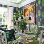 Bold green and black dining room featuring tropical fern wallpaper, a glass-top table with mixed-patterned seating, and a whimsical giraffe portrait.