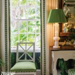 Window-side vignette showcasing tailored curtains with green trim, a white chair with green upholstery, and a sculptural white lamp with a green shade.
