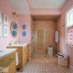 Bright and whimsical bathroom with coral-print wallpaper, wood-accented walk-in shower, blue wall decor, and coordinated patterned flooring and curtains.