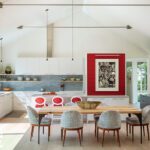 Airy modern kitchen with vaulted ceiling, open shelving, red accent chairs, and integrated dining area, flooded with natural light.