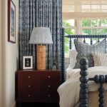 Traditional bedroom with navy spindle bed, patterned blue drapery, woven lamp, and layered pillows in classic New England style.