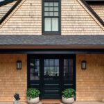 Classic New England exterior with cedar shingle siding, black-framed windows and door, and potted greenery on a welcoming porch.