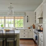 Light-filled kitchen with shaker cabinets, marble-topped island, spindle-back stools, and a wall of windows with tailored valances.