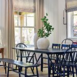 Modern farmhouse dining room with black spindle chairs, matching bench, and black table accented by neutral drapery and textured Roman shades.