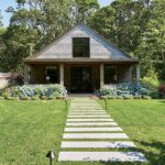 Charming New England cottage with weathered cedar shingles, symmetrical front porch, and a hydrangea-lined path leading to the entryway.