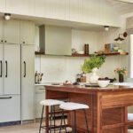 Contemporary kitchen featuring soft green cabinetry, a rich walnut island with waterfall edges, and open wood shelving against white shiplap walls.