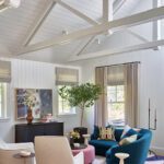 Bright and airy living room with vaulted ceilings, exposed white trusses, and colorful midcentury-inspired furniture on a graphic area rug.