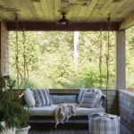 Relaxed covered porch with a hanging rope daybed, striped cushions, and woodland views, creating a tranquil outdoor retreat.