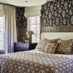 Elegant primary bedroom with botanical wallpaper, layered patterned bedding, and a mix of traditional and modern accents in neutral tones.