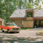 Rustic modern New England home with wood cladding, asymmetrical rooflines, and a vintage red pickup truck parked in a gravel drive.