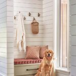 Welcoming mudroom with vertical shiplap walls, soft pink bench cushions, woven accessories, and a golden retriever sitting by the window.