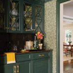 Moody green butler’s pantry with glass-front cabinets, floral wallpaper, and brass hardware in a traditional New England home.