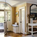 Welcoming entryway with striped wallpaper, arched glass door, built-in bench seating, and a star pendant light in a traditional home.
