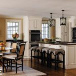 Classic white kitchen with paneled cabinetry, black accents, oversized island seating, and lantern-style pendant lights.