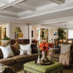 Comfortable living room with coffered ceiling, earth-tone furnishings, green ottoman, and views into the open kitchen and dining areas.
