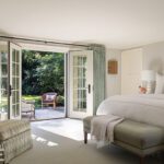 Serene primary bedroom with French doors opening to a private patio, featuring green upholstered furniture and soft neutral tones.