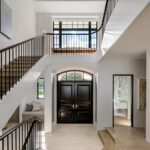 Sophisticated foyer with sweeping staircase, vaulted ceiling, and double front doors framed by natural light and architectural detailing.