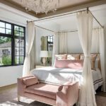 Romantic guest bedroom featuring a four-poster canopy bed, blush velvet bench, and soft neutral palette with elegant lighting and trim details.