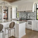 Bright kitchen with custom white cabinetry, a dramatic hexagonal tile backsplash, wood floors, and polished chrome barstools at the island.