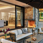 Stylish covered patio with cozy lounge seating, stone fireplace, and indoor-outdoor flow through large sliding glass doors to the home’s living area.