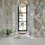 Luxe powder room featuring a curved wall covered in metallic mosaic tile, crystal chandelier, and a modern vessel sink beneath a narrow window.