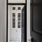 Sleek hallway with black doors, patterned tile floor, and a view into a guest bath with white cabinetry and decorative glass inserts.