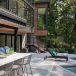 Sleek outdoor patio with poolside lounge area, marble-topped bar, and garden views, designed for modern entertaining.