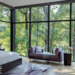 Serene primary bedroom with panoramic glass walls overlooking the forest, furnished with soft textures and muted tones.