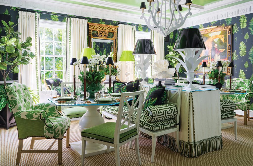 Bold green and black dining room featuring tropical fern wallpaper, a glass-top table with mixed-patterned seating, and a whimsical giraffe portrait.