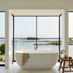 Freestanding bathtub with panoramic ocean views framed by floor-to-ceiling windows.