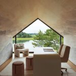 Stylish attic home office with pitched ceiling and lake view through triangular window.