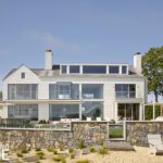 Rear view of a modern coastal home with expansive glass windows and outdoor living spaces.