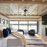Luxurious primary bedroom with tufted headboard, fireplace, and coastal view