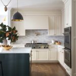 Stylish kitchen with cream cabinetry, professional range, and gold pot filler under a custom hood