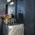 Moody powder room with marble waterfall vanity and brass mirror against deep blue plaster walls