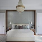 Elegant primary bedroom with beaded chandelier, upholstered bed, and soft blue-gray palette.