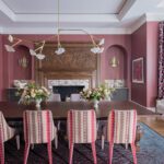 Bold dining room with red walls, ornate wood fireplace surround, and patterned dining chairs under sculptural lighting.