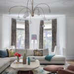 Living room with modern sectional, patterned rug, sculptural chandelier, and large bay window.