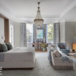 Sophisticated primary bedroom with bay window, chandelier, neutral-toned furnishings, and a fireplace seating area.