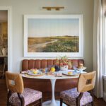 Stylish banquette breakfast nook with leather bench, tulip table, and scenic artwork.