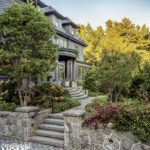Grand stone entry with curved stairs and lush landscaping in front of a gray traditional-style home.