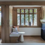 Cozy inglenook with stained glass windows, wood paneling, and built-in seating beside a fireplace.
